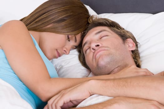 Close-up of a mid adult man sleeping on the bed with a young woman