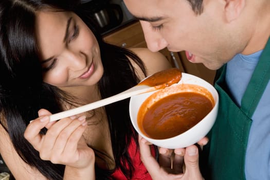 Close-up of a young woman feeding tomato soup to a mid adult man in the kitchen