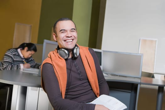 Portrait of a young man sitting in a computer lab and laughing