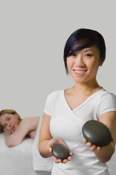 Close_up of a massage therapist holding two pebbles with a mature woman lying on a massage table behind her