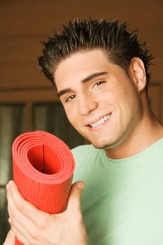 Portrait of a young man holding a rolled up exercise mat