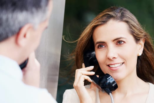Mid adult woman talking on a pay phone with a mid adult man in front of her