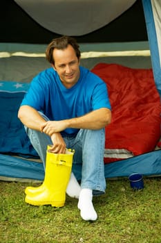 Close-up of a mature man sitting in a tent holding galoshes