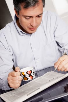 Close-up of a mature man holding a cup of coffee and doing a crossword puzzle