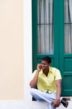 Young man sitting in front of a door and talking on a mobile phone