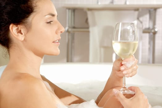 Side profile of a young woman holding a glass of wine in a bathtub