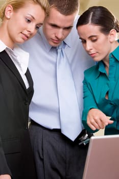 Close-up of two businesswomen and a businessman looking at a laptop