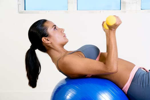 Side profile of a young woman exercising with dumbbells on a fitness ball