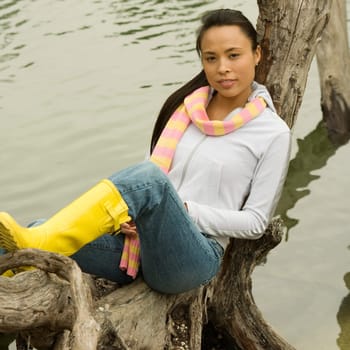 Portrait of a young woman sitting on a tree trunk by the lake