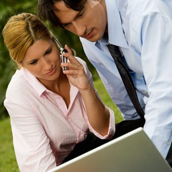 Close-up of a businessman and a businesswoman working on a laptop and talking on a mobile phone