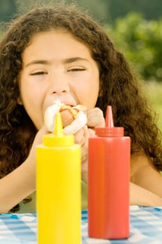 Close-up of a girl eating a burger behind sauce bottles