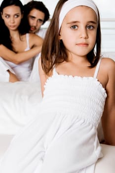 Portrait of a girl reclining on the bed with her parents sitting behind her