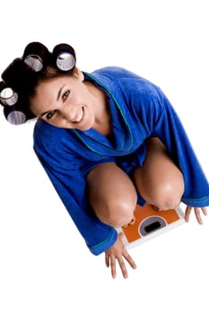 Portrait of a young woman with curlers in her hair crouching on a weight scale