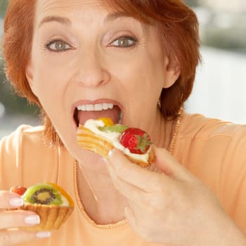 Portrait of a senior woman eating a fruit tart