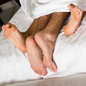 High angle view of a coupleŽs feet under the sheets of a bed