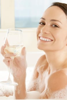 Portrait of a young woman holding a glass of white wine in the bathtub