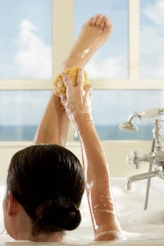 Rear view of a young woman in a bathtub using a bath sponge