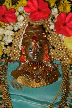 View of golden, metallic icon of Devi Mahalakshmi decorated with pearls, jewellery and flowers