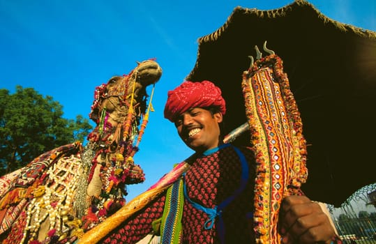 Young man holding a trident and standing near a camel, Jaipur, Rajasthan, India