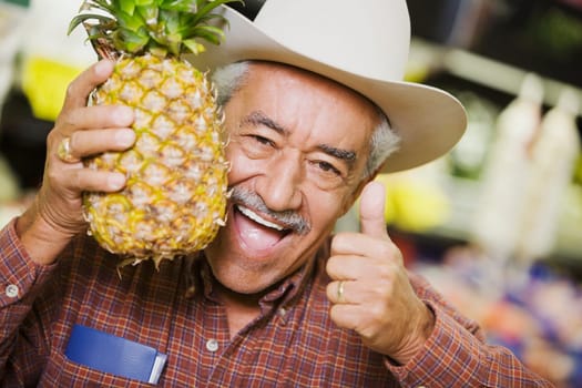 Portrait of a senior man holding a pineapple and showing a thumbs up sign