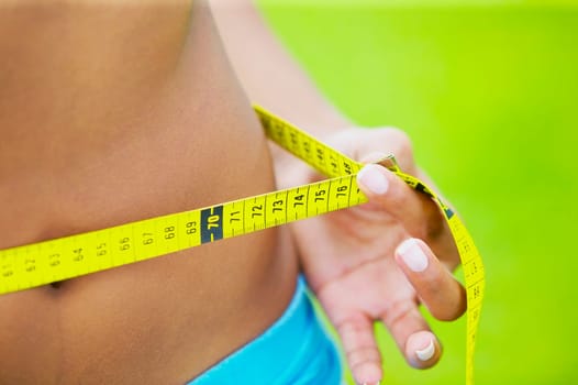 Mid section view of a woman measuring her waist with a tape measure