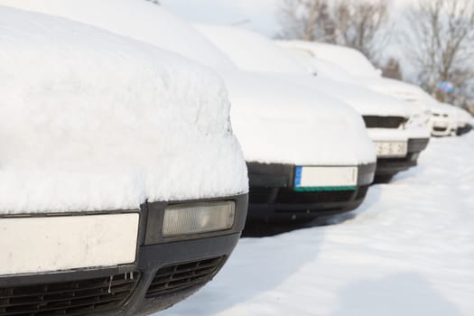 Snow covered cars parked in a row next to each other. Cars on the street in cold winter.