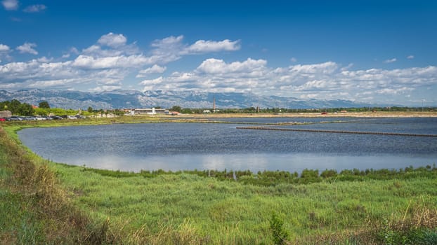 Phishing ponds or lake and small industrial estate in Nin with beautiful mountain range of Dinaric Alps in the background, Croatia