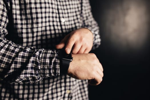 Man in casual clothes clicks hand watches, bracelet, black blurred background. High quality photo