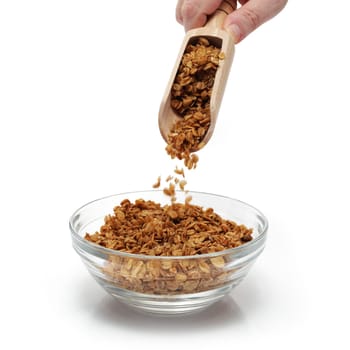 Granola being emptied from a scoop into a glass breakfast bowl