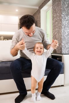 Father teaching a baby to walk in living room at home. First child steps
