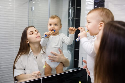 Full of proud mother looking at her baby son brushing his teeth in bathroom