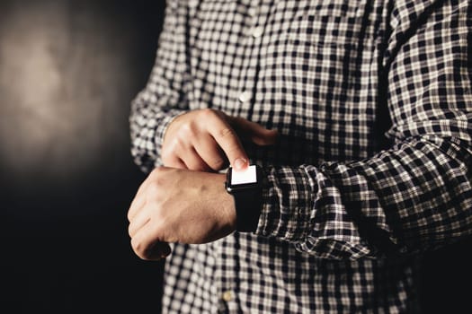 Man in casual clothes clicks hand watches, bracelet, black blurred background. High quality photo
