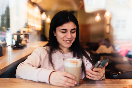 Girl smiling, drinks coffee in cafe and reading phone. Blurred background. High quality photo