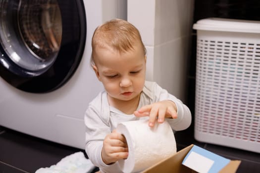 Toddler boy plays with toilet paper.
