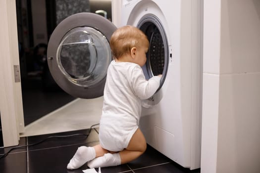 Child climbing into front-loading washing machine. Side view. Lack of parental supervision.