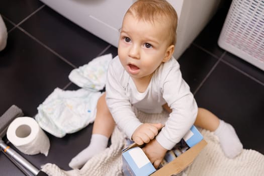 Infant boy open box with tablet for dishwasher or detergent in bathroom alone.