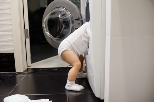 Child climbing into front-loading washing machine. Side view. Lack of parental supervision.