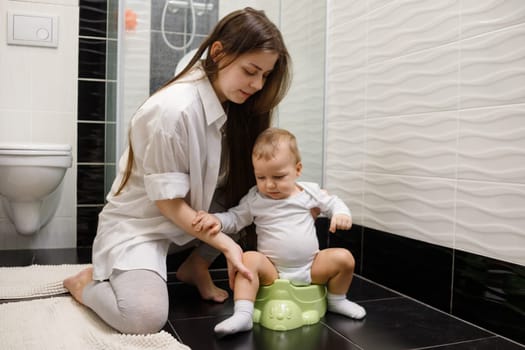 Mom try to sitt infant baby on bedpan in bathroom