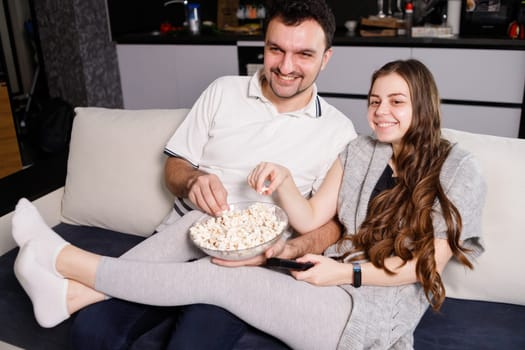 Happy couple eating popcorn and watching tv at home.