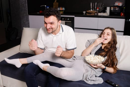 Man emotionally watching sport game, his girl eating popcorn.