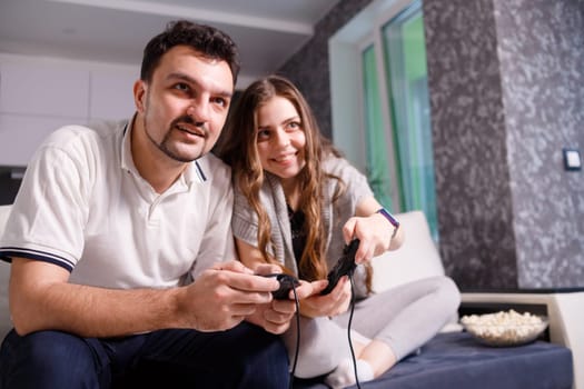 Young couple playing video games sitting on sofa in livingroom at home.
