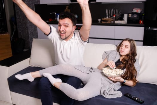 Man emotionally watching sport game, his girl eating popcorn.