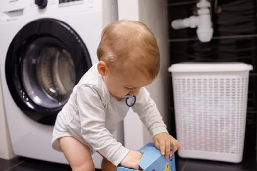 Infant boy open box with tablet for dishwasher or detergent in bathroom alone. Children without parental supervision
