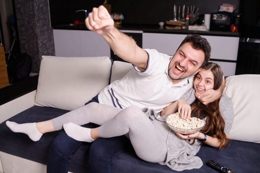 Man emotionally watching sport game, his girl eating popcorn.