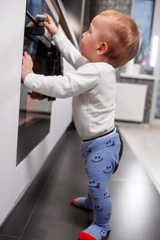 Little child playing with electric stove in kitchen