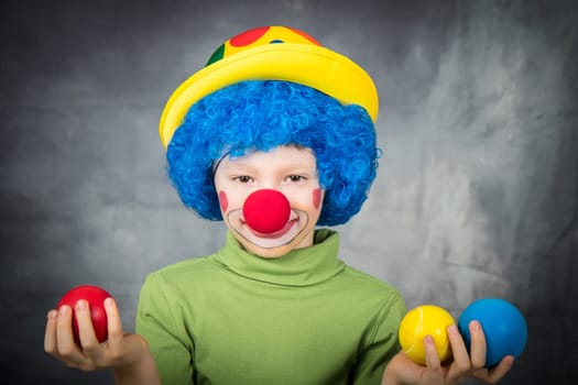 young child dressed as a clown with wig and fake nose has fun playing with colorful balls celebrating carnival