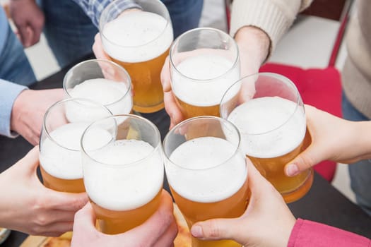 Group of happy friends drinking and toasting beer at  home