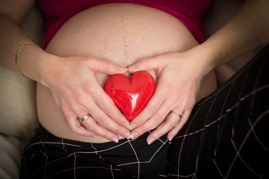 pregnant woman holding a red heart  on her belly. vintage style