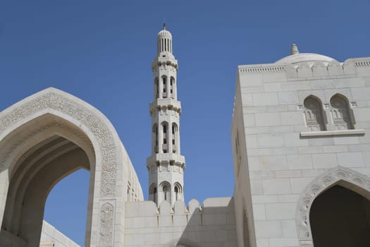 Archway with the Arabic inscription Sultan Qaboos Grand Mosque and the main minaret. It is considered to be one of the most important buildings in the Sultanate of Oman.