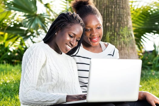 Close up outdoor portrait of two African teen girls typing on laptop in park.